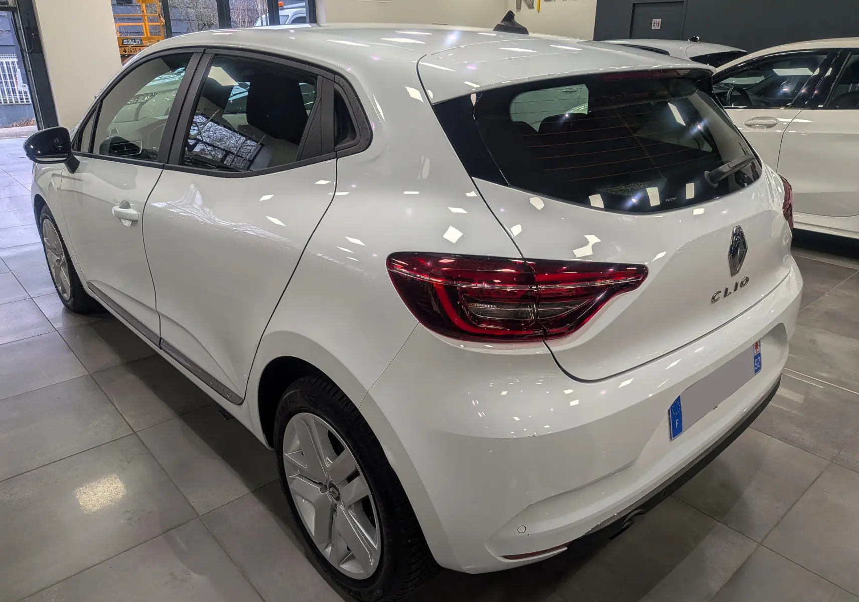 Vue 3/4 arrière droite d'une Renault Clio V Business blanche Glacier, avec feux arrière LED et jantes alliage.