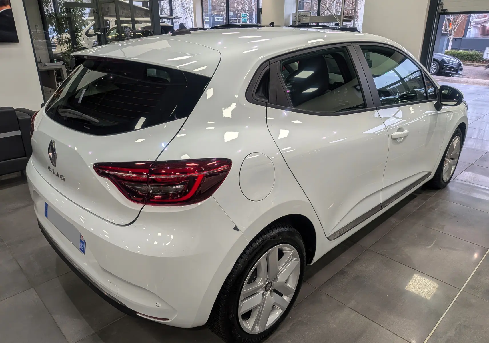 Vue 3/4 arrière droite d'une Renault Clio V blanc glacier en showroom, avec feux arrière LED et jantes alliage.