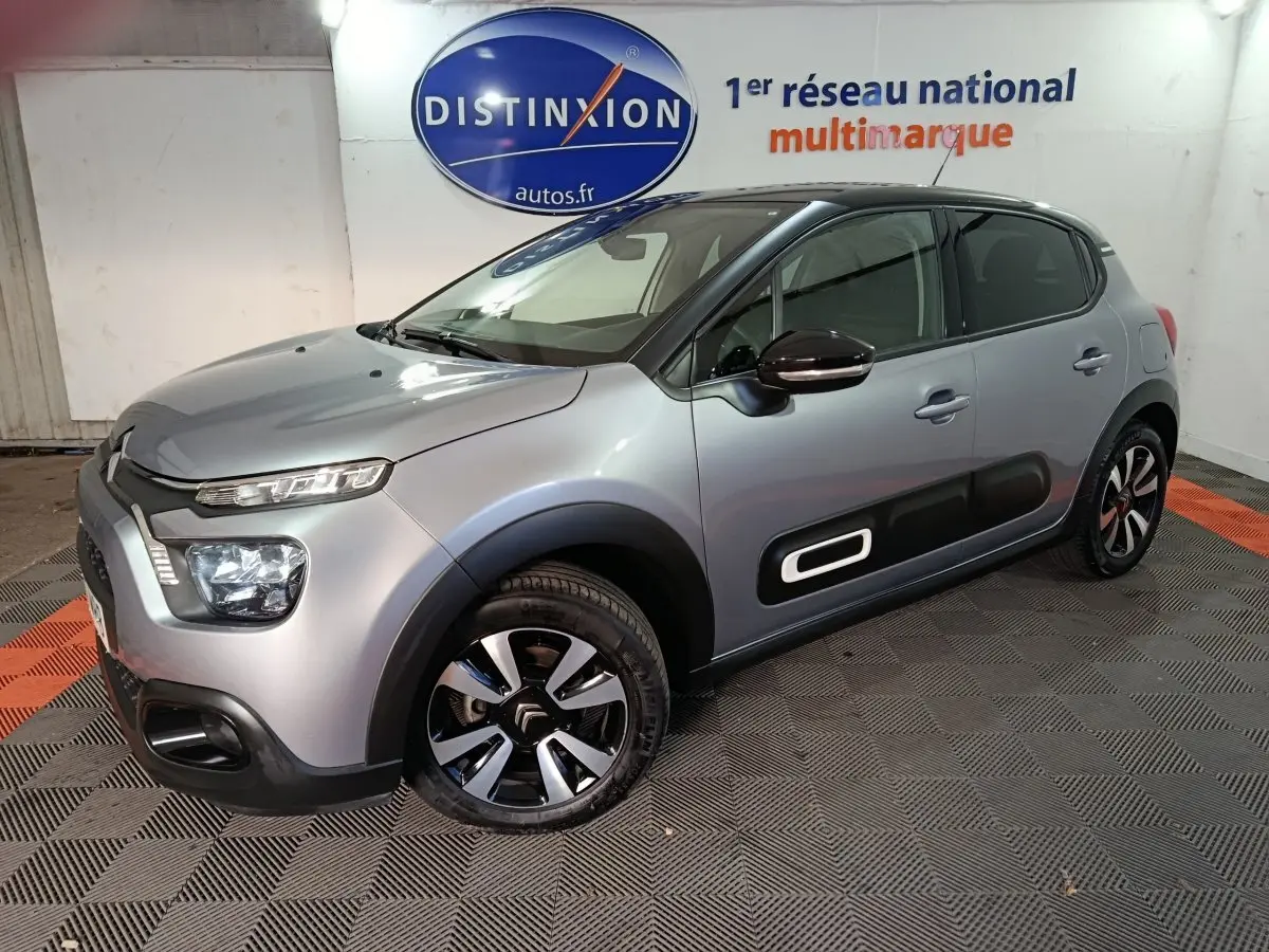 Citroën C3 gris foncé vue 3/4 avant droit, avec protections latérales noires et jantes bicolores distinctives.