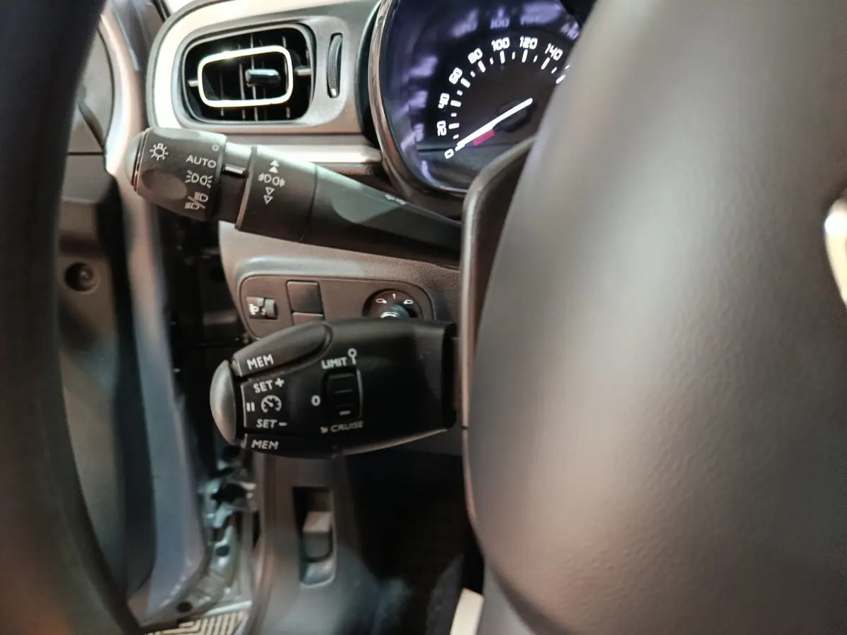 Gros plan sur la colonne de direction et commandes du volant d’une Citroën C3 gris foncé, tableau de bord partiellement visible.