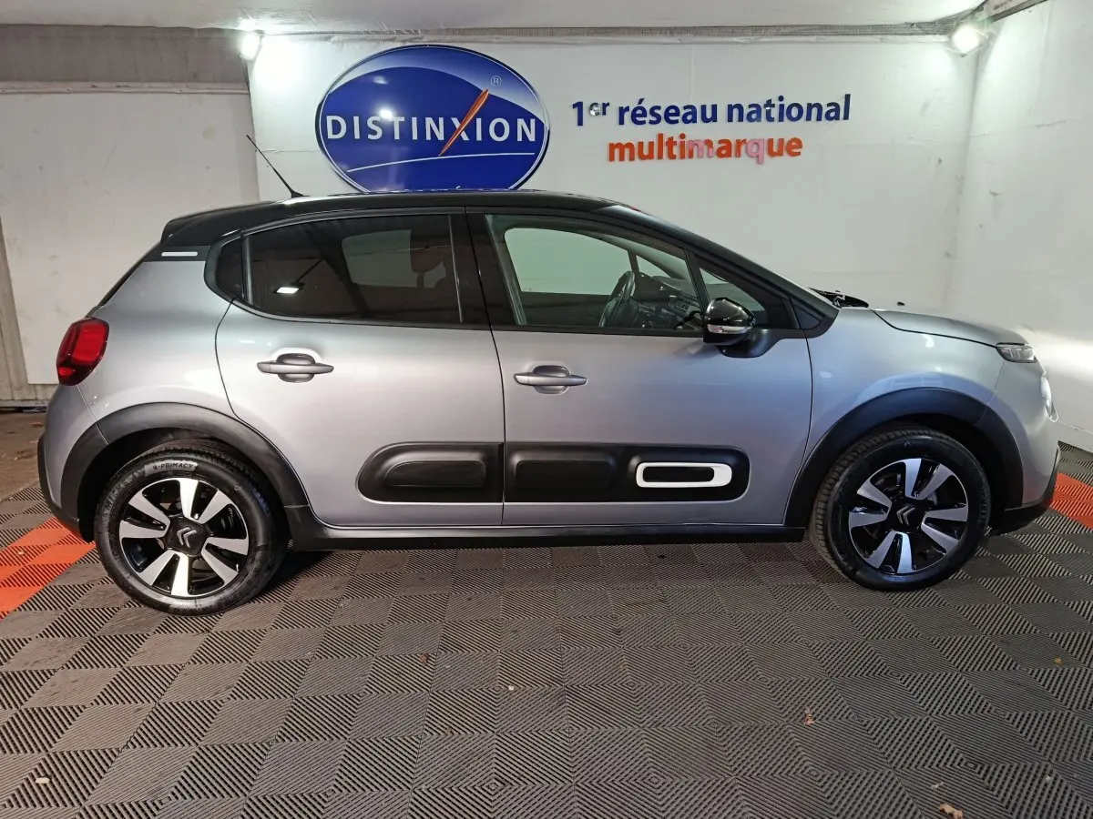 Profil droit d'une Citroën C3 gris foncé 2024 avec protections latérales noires et jantes bicolores dans un showroom.
