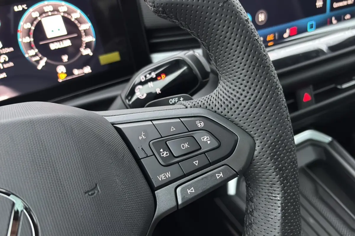 Gros plan sur le volant cuir perforé du Volkswagen T-Roc 2026 avec commandes multifonctions et levier de vitesses DSG visible.