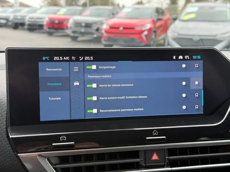 Écran tactile central du Citroën C4 X 2024 affichant les réglages d’aides à la conduite, avec vue floue sur des voitures en arrière-plan.