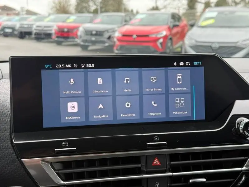 Vue intérieure centrée sur l'écran tactile du tableau de bord d'un Citroën C4 X gris 2024, avec plusieurs véhicules flous en arrière-plan.