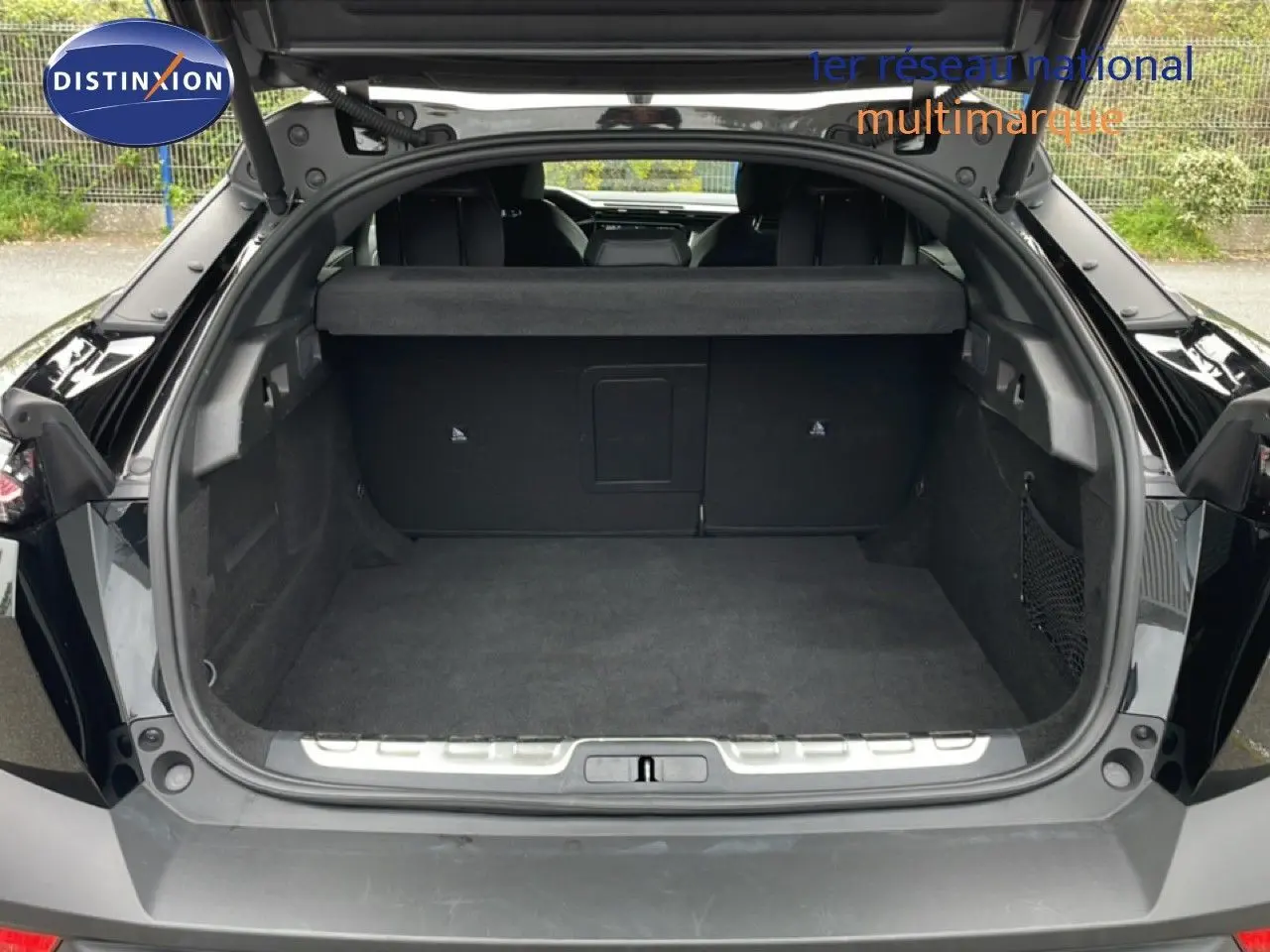 Coffre ouvert vu de l'arrière d'une Peugeot 408 HYBRID 145CH GT noir métal, montrant un espace de chargement spacieux.