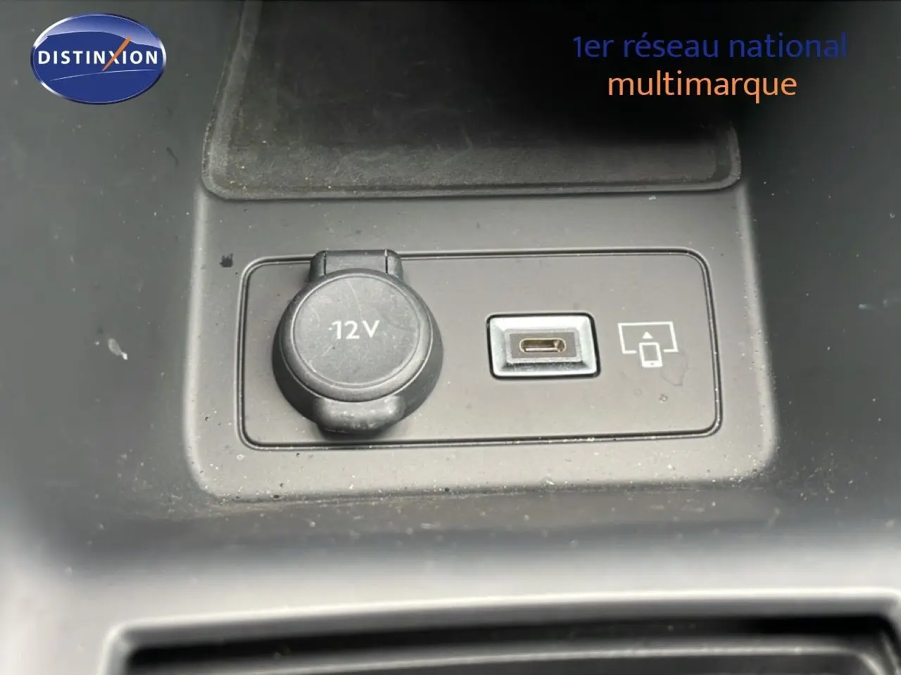 Gros plan sur la prise 12V et port USB-C du Peugeot 408 Hybrid 145ch GT noir métal, intérieur visible en arrière-plan.
