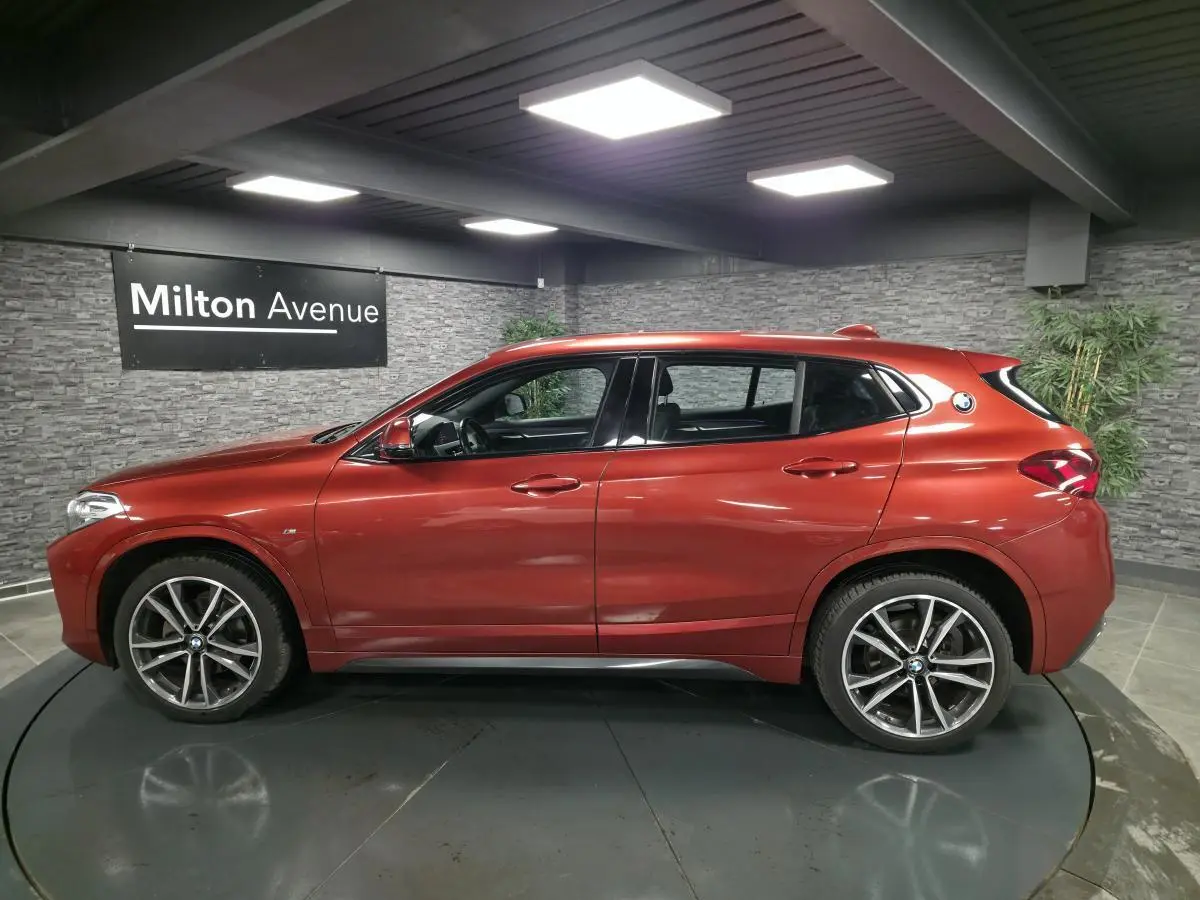 BMW X2 sDrive 18d M Sport orange métallisé vue de profil côté gauche en intérieur avec jantes 19 pouces M.