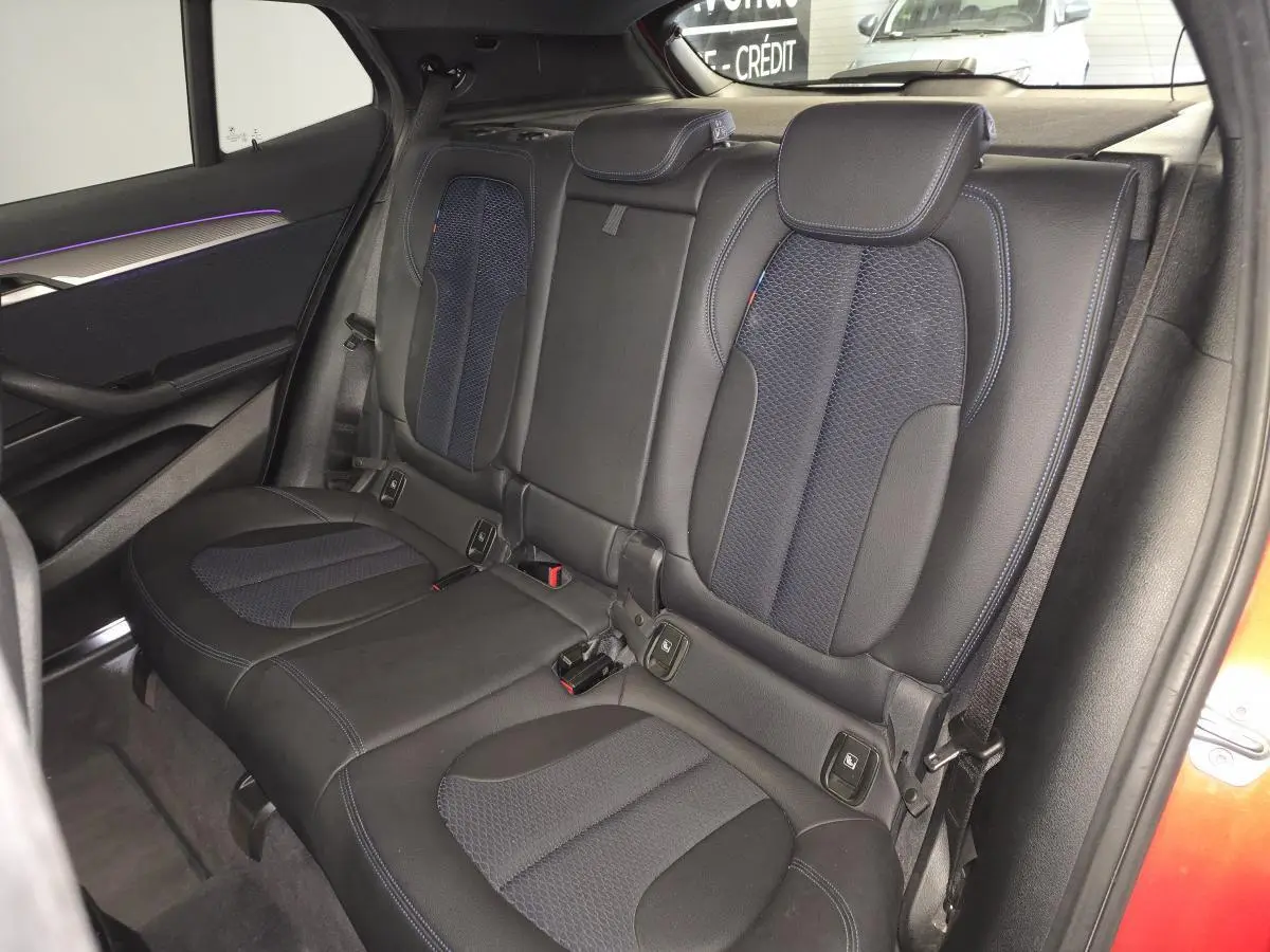 Vue intérieure de la banquette arrière du BMW X2 orange, avec sellerie tissu et similicuir noir et bleu, et inserts décoratifs.