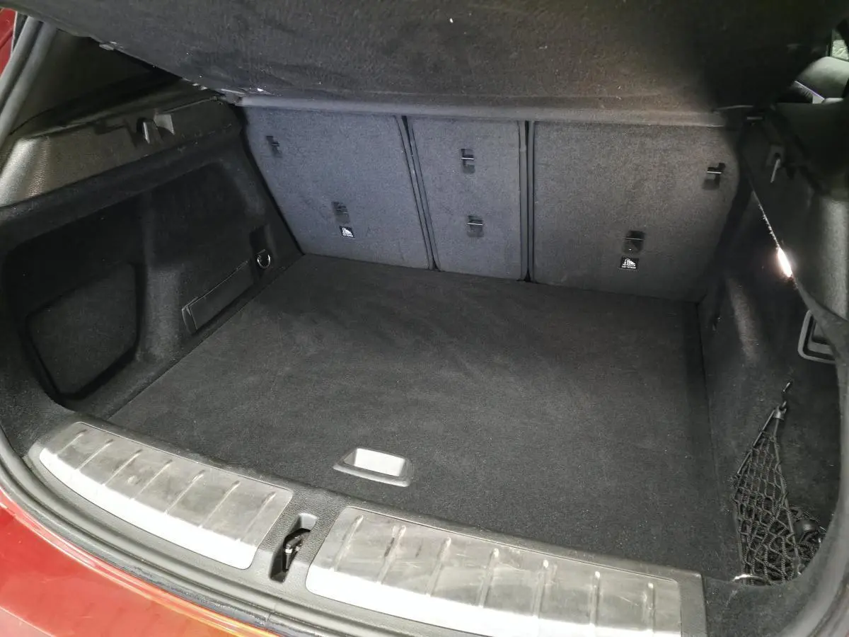Coffre ouvert de BMW X2 orange, vue intérieure montrant tapis noir et filet de rangement latéral.