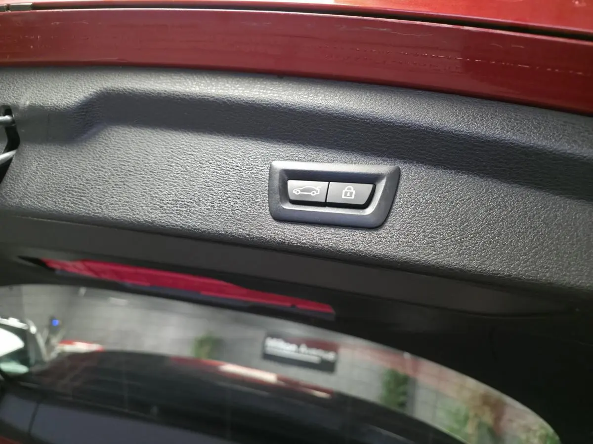Bouton de fermeture électrique du hayon sur la partie intérieure du coffre d'une BMW X2 orange.
