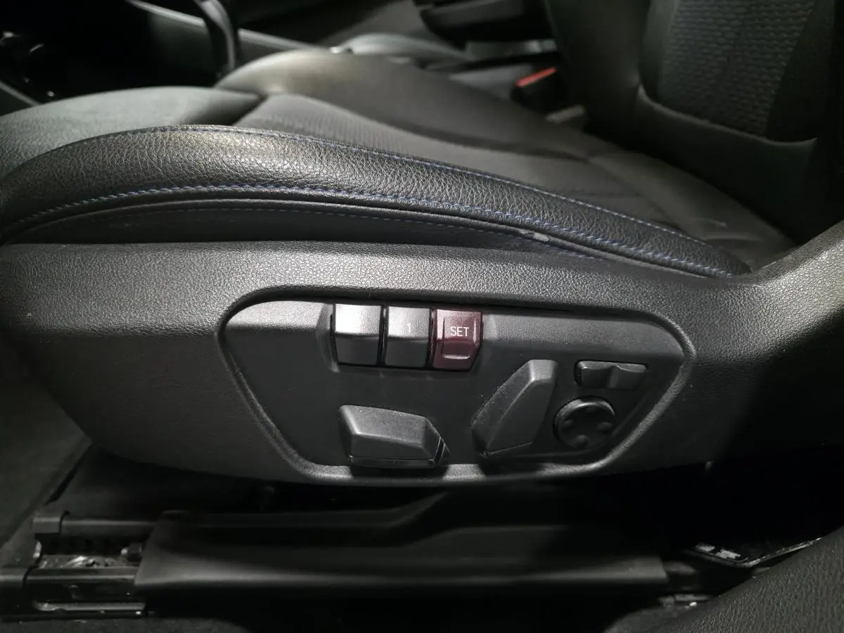 Gros plan sur les commandes électriques de réglage du siège conducteur en similicuir noir avec surpiqûres bleues d'une BMW X2 M Sport 2021.