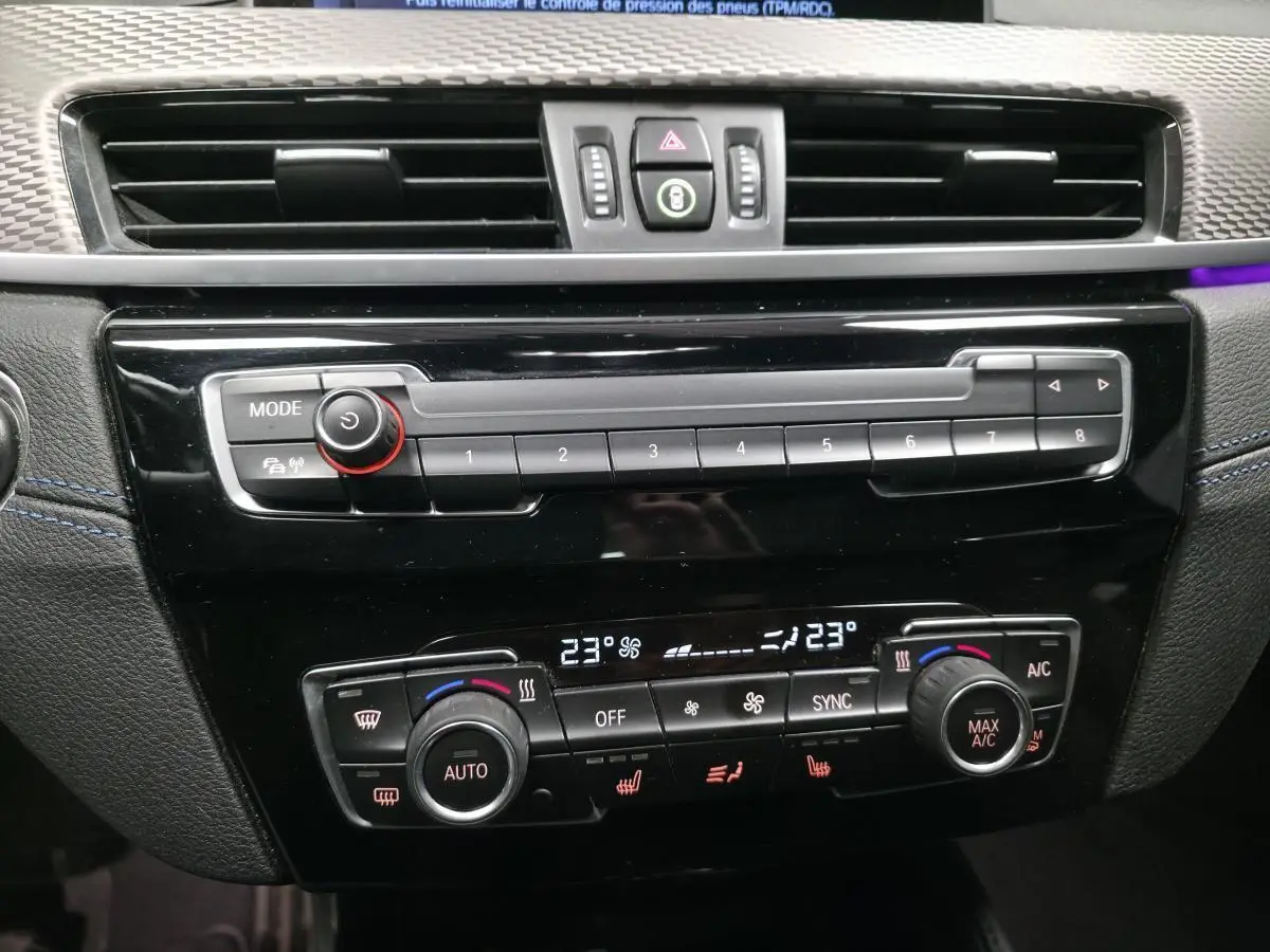 Vue rapprochée de la console centrale noire du BMW X2 avec commandes climatisation automatique bi-zone et autoradio.