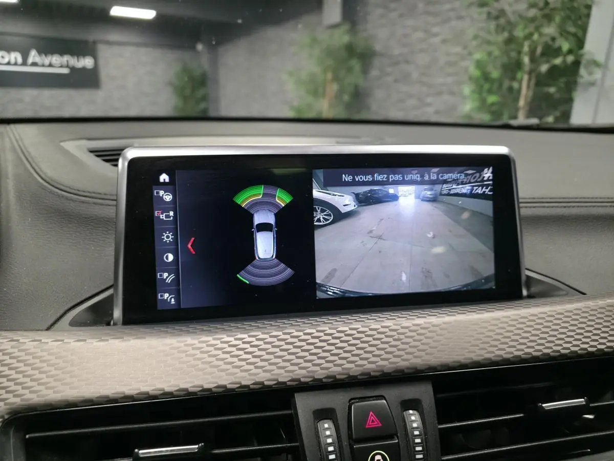 Écran central de BMW X2 orange montrant la caméra de recul et l’aide au stationnement en intérieur.