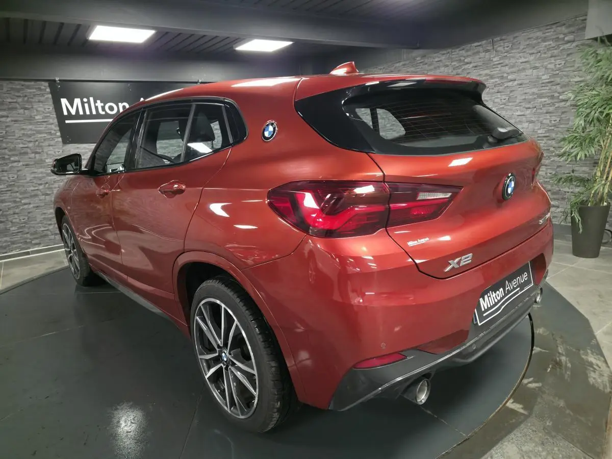 Vue 3/4 arrière droite d'une BMW X2 orange métallisée avec jantes alliage et double sortie d'échappement chromée.