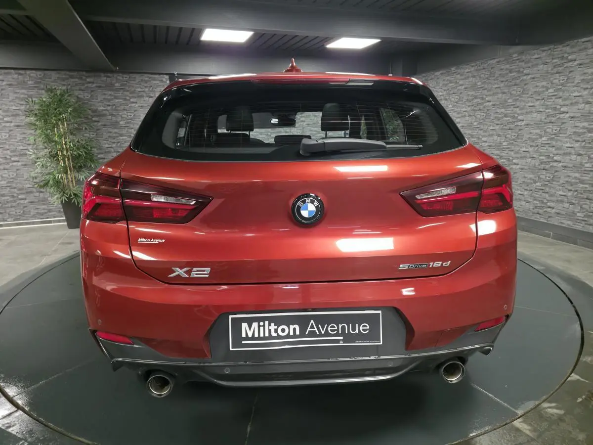 Vue arrière d'une BMW X2 sDrive 18d orange métallisée avec double sortie d'échappement et logo M Sport visible.