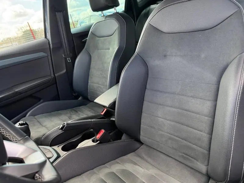 Vue intérieure rapprochée des sièges avant en tissu et cuir noir du SEAT Arona 2025, avec console centrale visible.