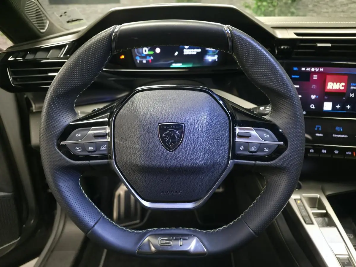 Vue rapprochée du volant cuir perforé noir avec badge GT et tableau de bord numérique de la Peugeot 408 2025.