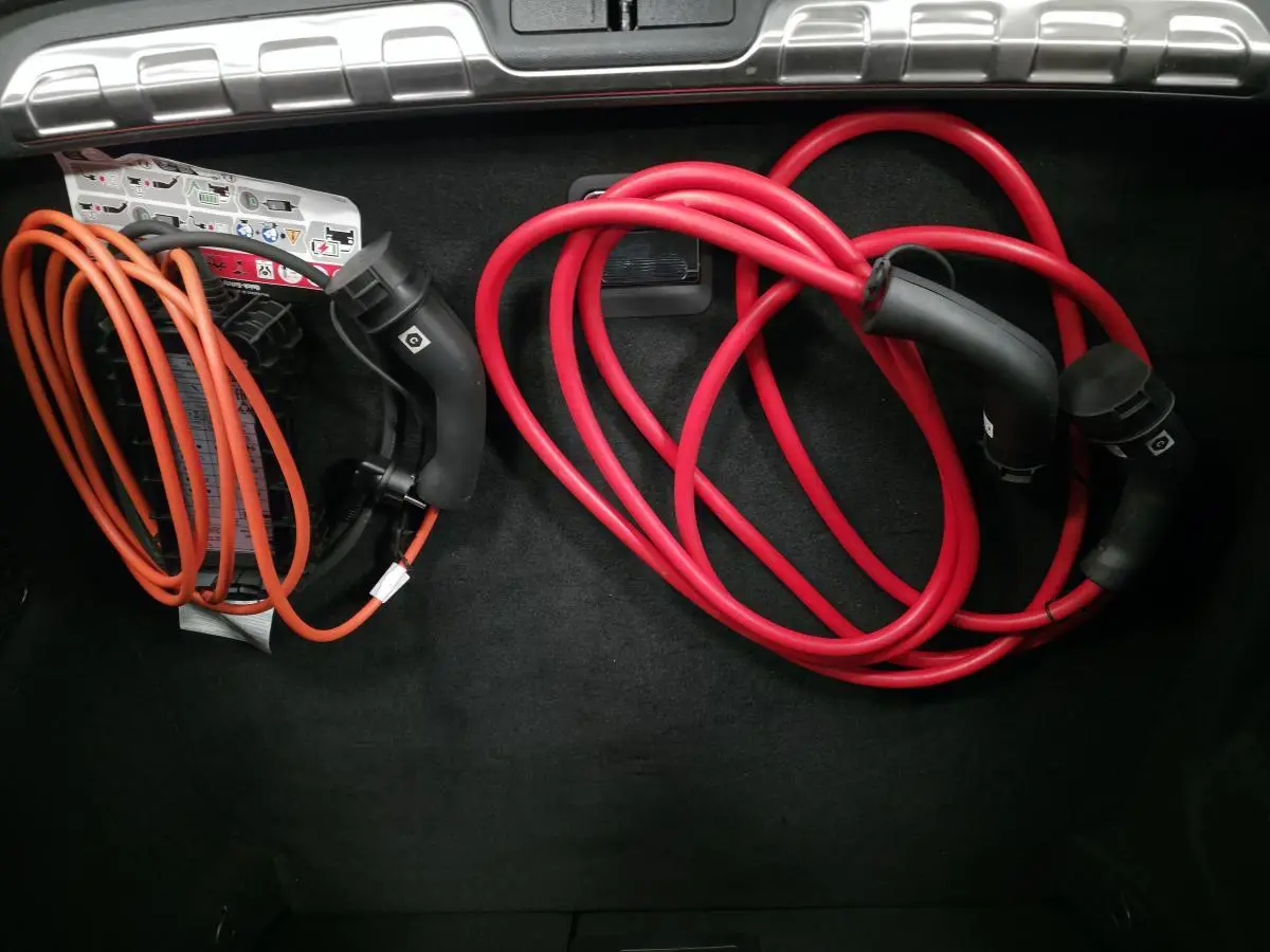Coffre ouvert du Peugeot 408 gris avec câbles de recharge rouge et orange rangés sur le tapis noir.