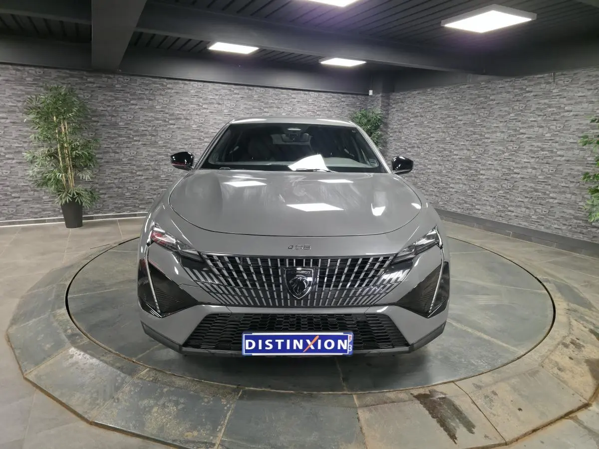Vue frontale d'une Peugeot 408 gris métallisé avec calandre verticale et phares LED distinctifs en intérieur showroom.