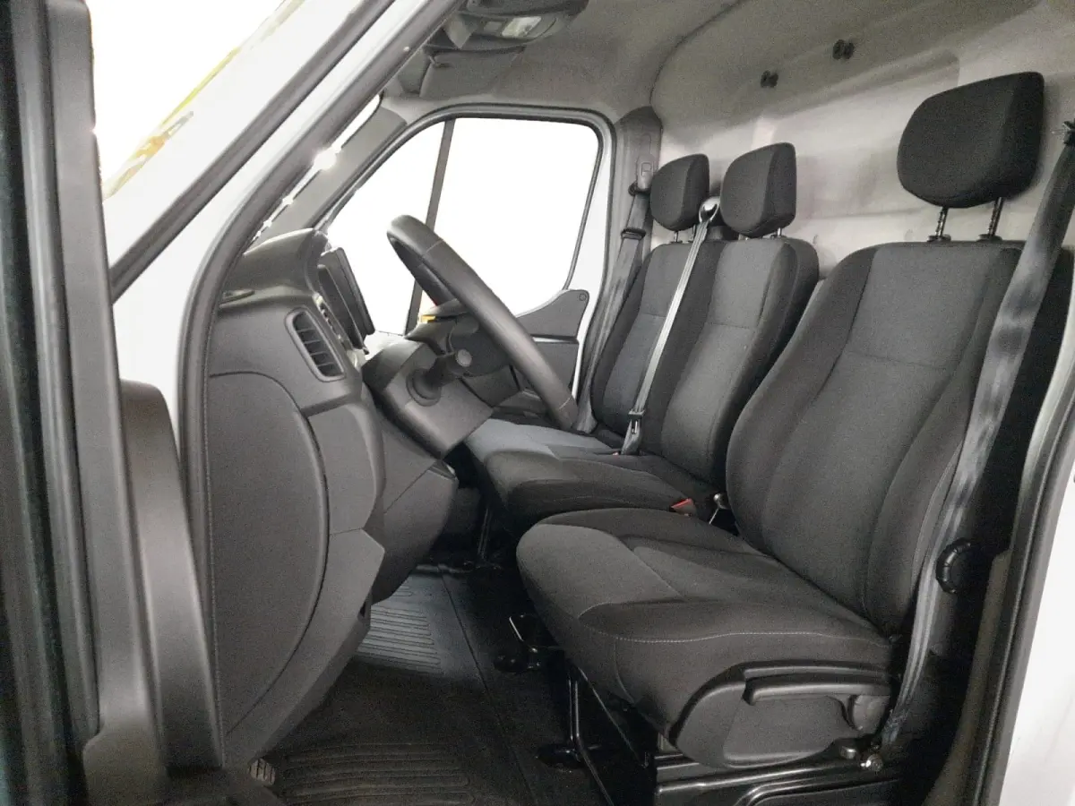 Vue intérieure côté conducteur du Renault Master 2024 blanc, montrant les sièges avant en tissu noir et le volant réglable.