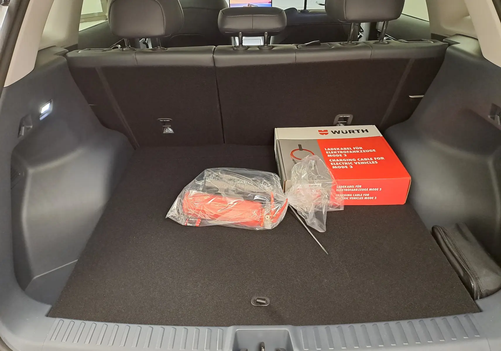 Coffre spacieux du Geely E5 PRO gris Moonlight vu de l'arrière avec câble de recharge électrique Würth posé à l'intérieur.