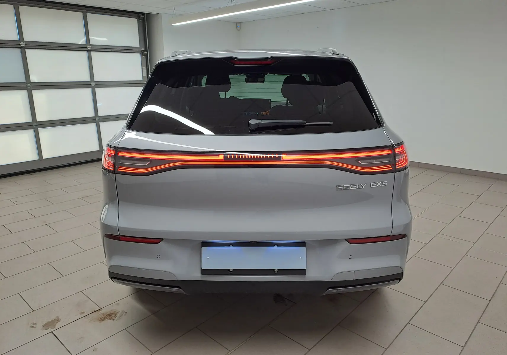 Vue arrière d'un SUV électrique Geely E5 PRO gris Moonlight de 2026 avec feux arrière LED continus allumés en intérieur.
