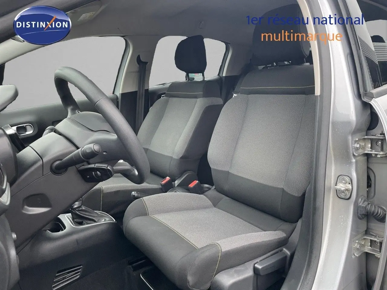Vue intérieure côté conducteur de la Citroën C3 2023 gris acier, sièges tissu gris et noir avec coutures contrastées.