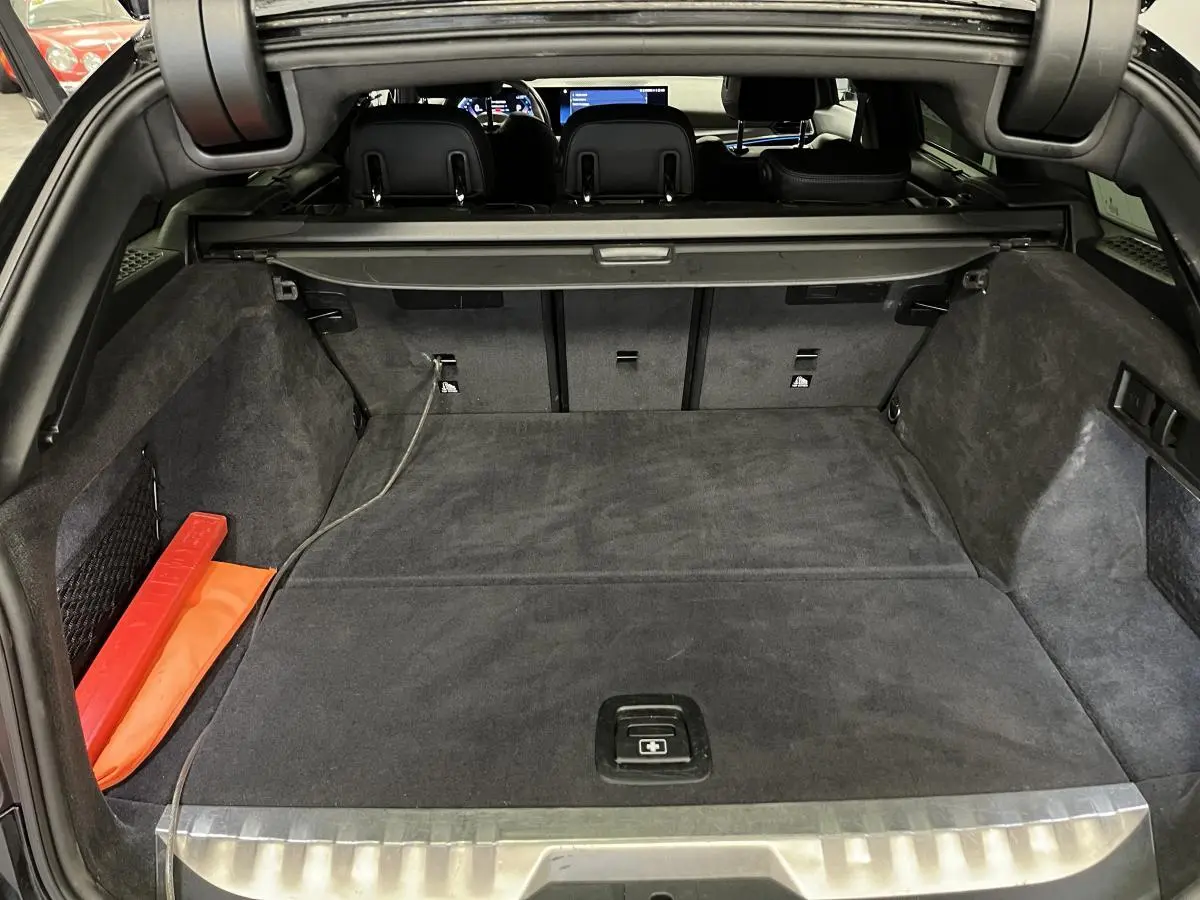 Coffre ouvert vu de l'arrière d'une BMW Série 3 Touring 320e noire, avec tapis et cache-bagages gris foncé.