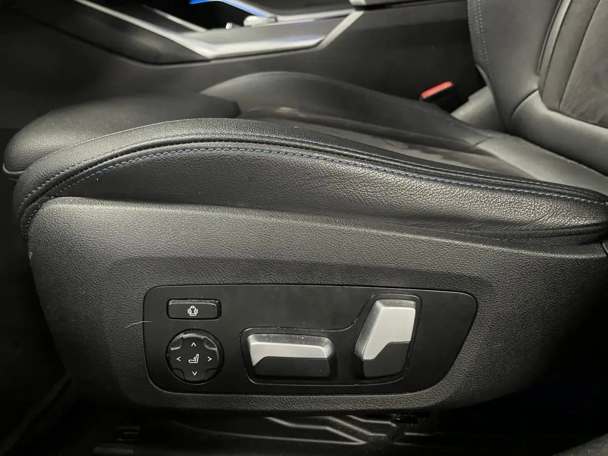 Gros plan sur les commandes électriques noires et argentées de l'appui lombaire côté conducteur d'une BMW Série 3 Touring noire.