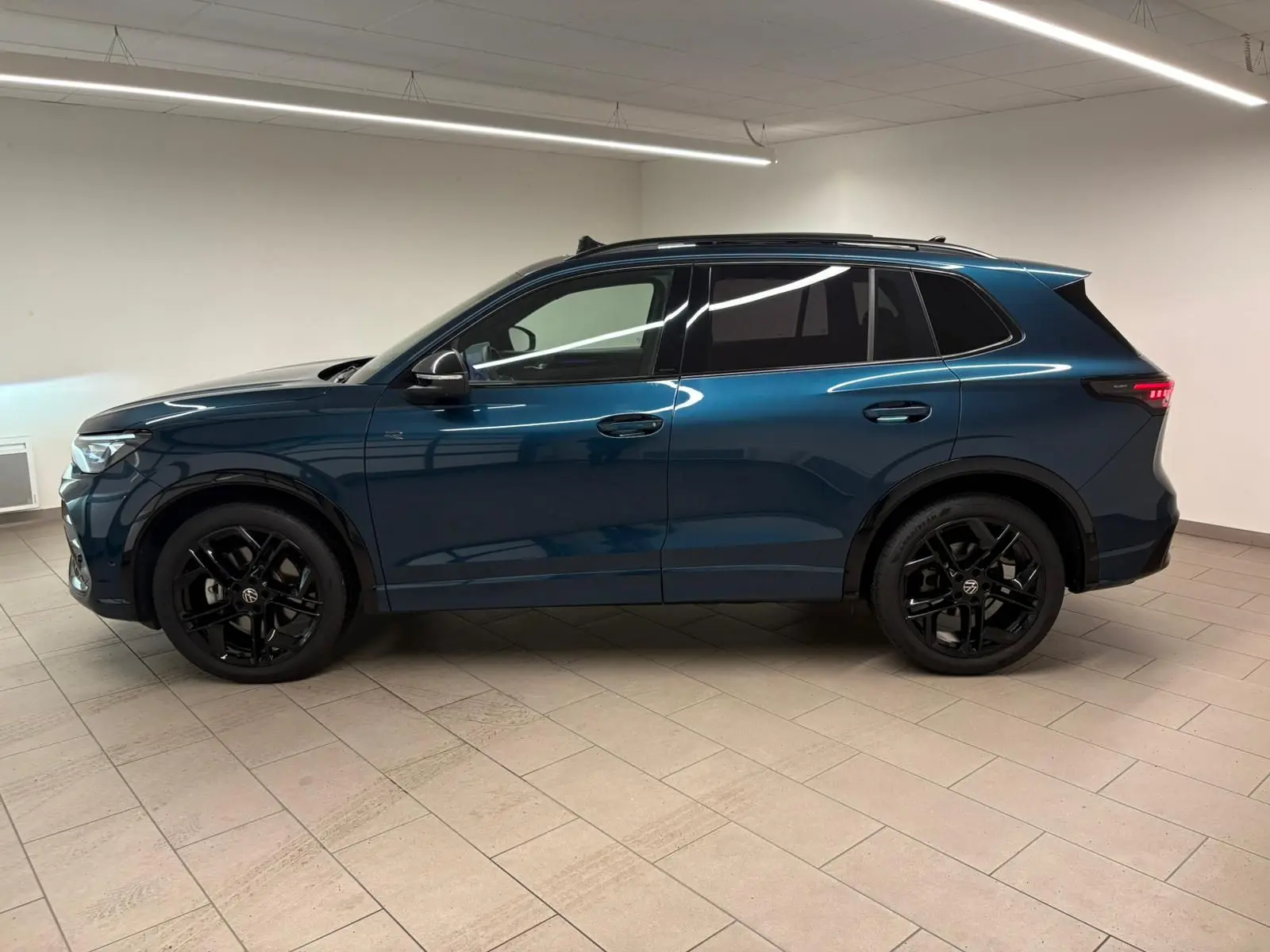 Vue de profil côté gauche du Volkswagen Tiguan 2024 en Nightshade Blue avec jantes noires et vitres surteintées.