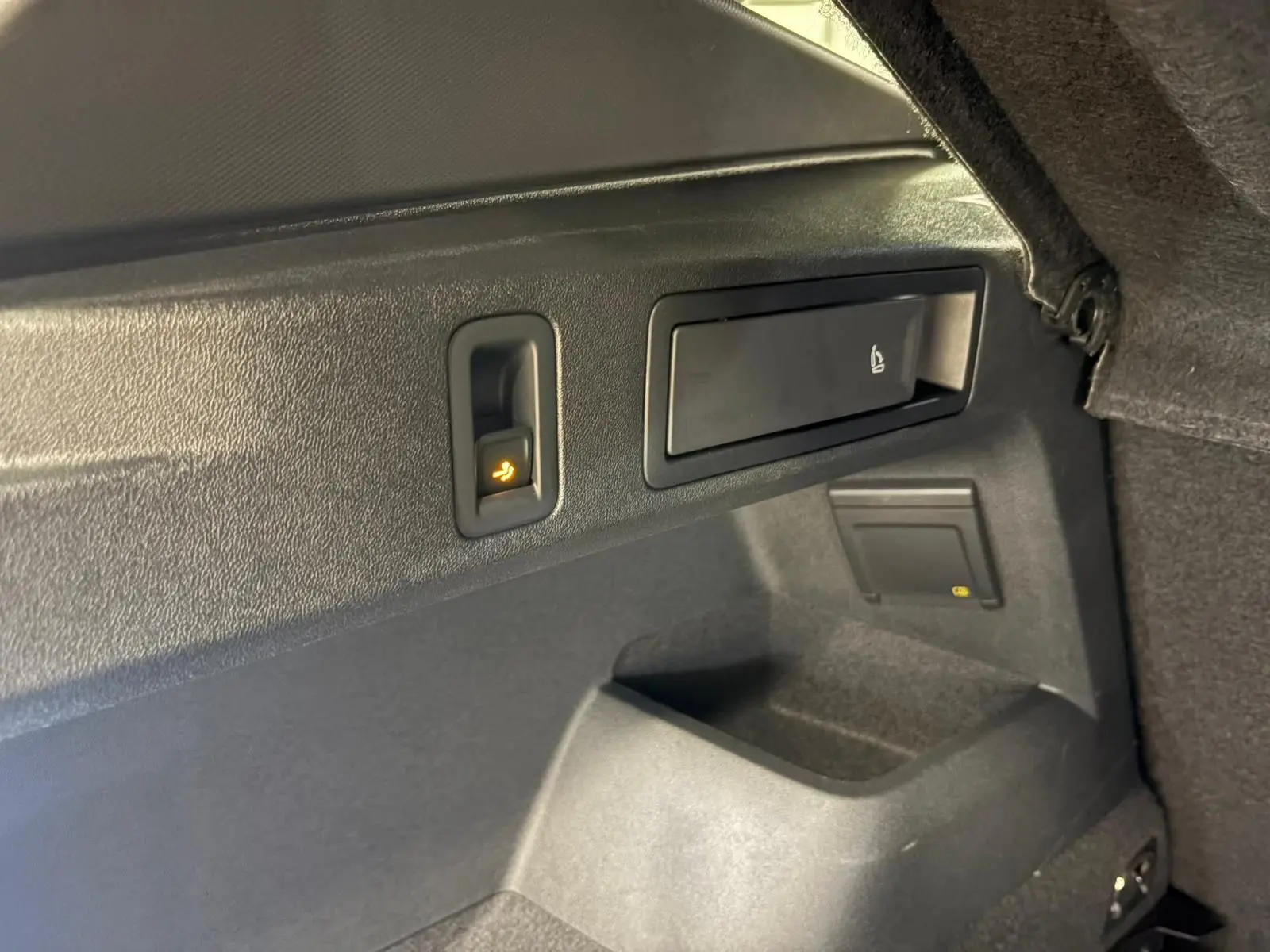 Détail intérieur du coffre du Volkswagen Tiguan 2024, montrant les commandes de rabattement des sièges en plastique noir.