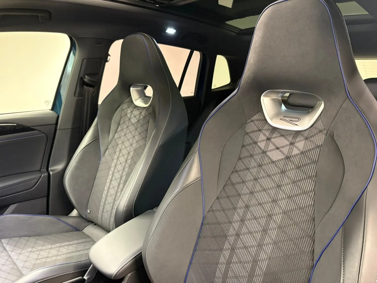 Vue intérieure rapprochée des sièges avant en cuir gris avec surpiqûres bleues du Volkswagen Tiguan 2024.