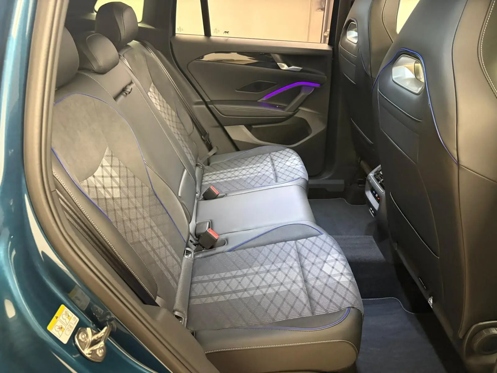 Vue intérieure côté gauche des sièges arrière du Volkswagen Tiguan 2024 en Nightshade Blue avec surpiqûres bleues et éclairage d'ambiance violet.