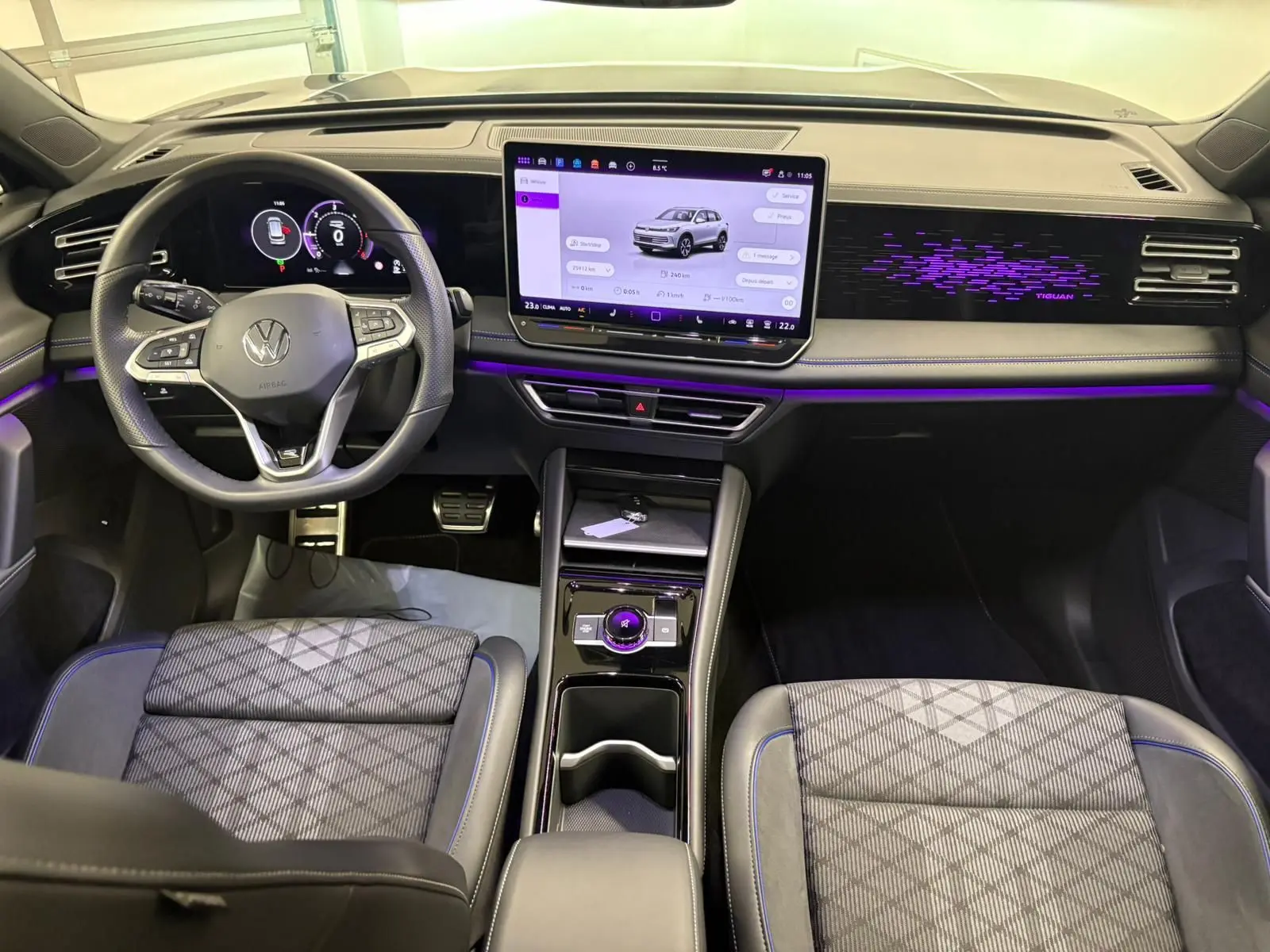 Vue intérieure avant du Volkswagen Tiguan 2024 avec tableau de bord numérique, écran tactile central et éclairage d'ambiance violet.