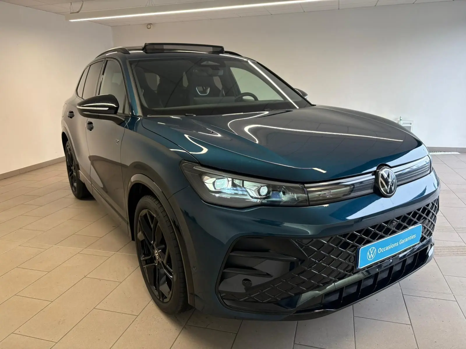 Volkswagen Tiguan 2024 Nightshade Blue en 3/4 avant droit, jantes noires et calandre R-Line noire visible.
