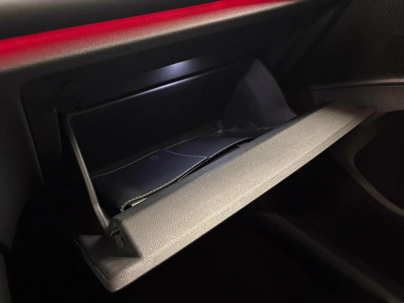 Gros plan sur la boîte à gants ouverte du Volkswagen Tiguan 2024, intérieur noir avec éclairage rouge ambiant.