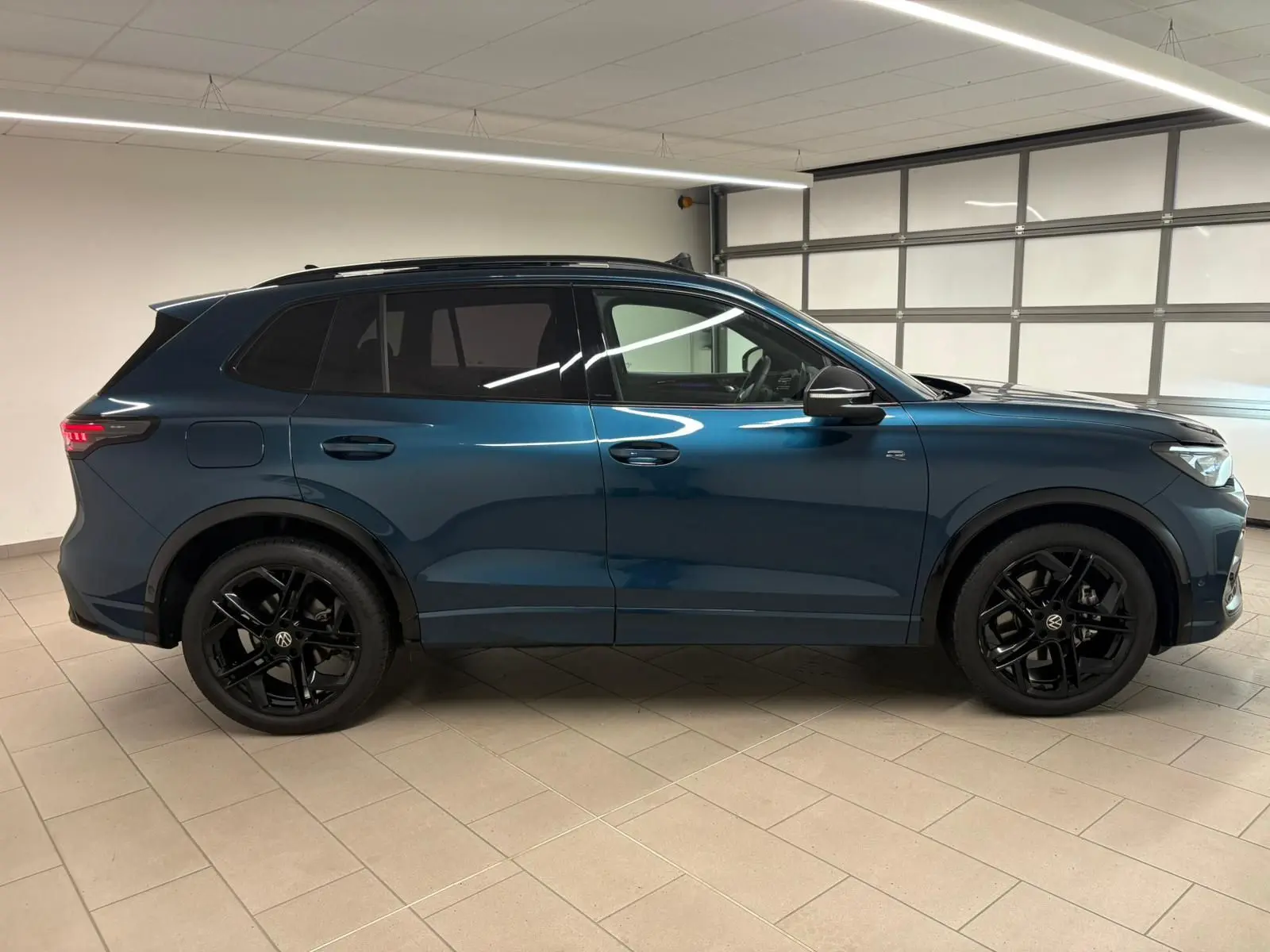 Vue de profil côté gauche d'un Volkswagen Tiguan 2024 en Nightshade Blue avec jantes noires et toit ouvrant panoramique.