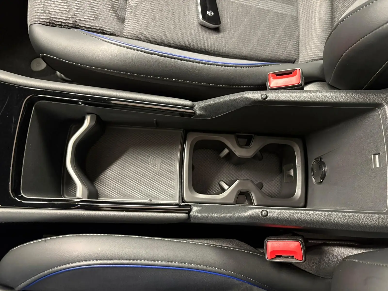 Vue plongeante sur la console centrale du Volkswagen Tiguan 2024, avec porte-gobelets et sellerie noire aux surpiqûres bleues.
