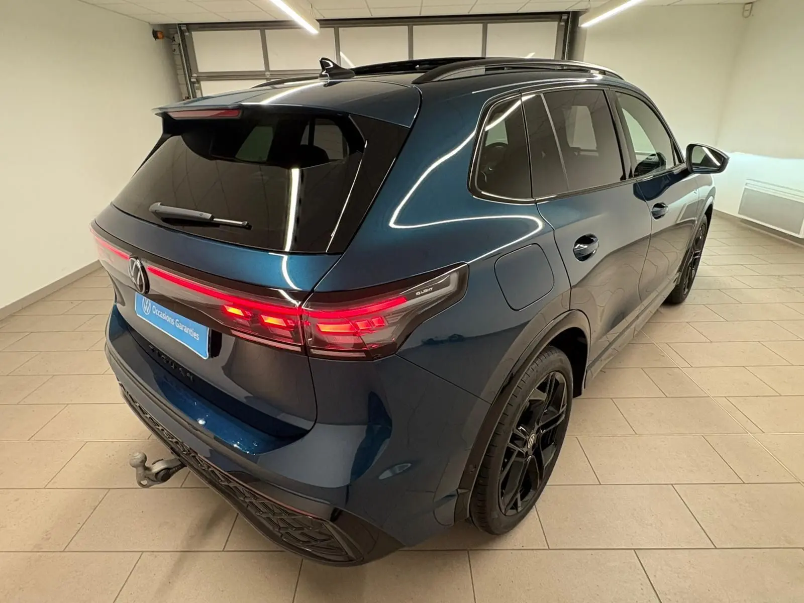Vue 3/4 arrière droite du Volkswagen Tiguan 2024 Nightshade Blue avec jantes noires et attelage escamotable.