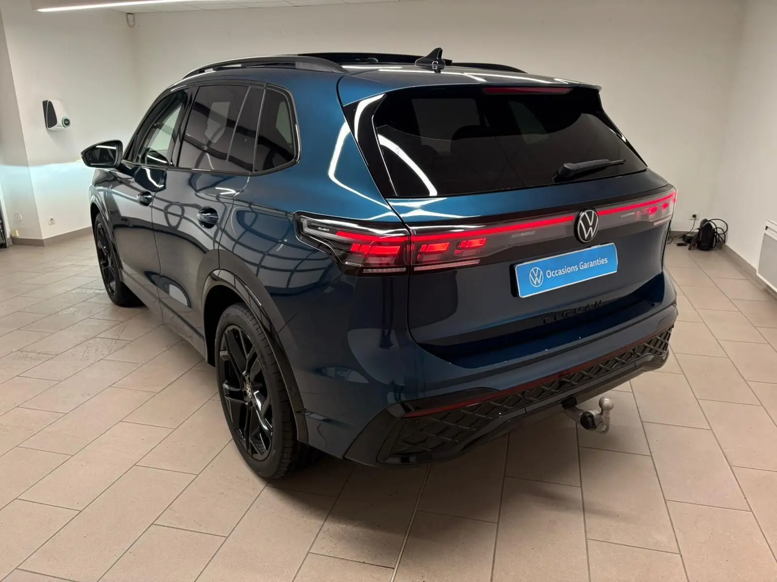 Vue 3/4 arrière du Volkswagen Tiguan 2024 en Nightshade Blue avec jantes noires et attelage escamotable.