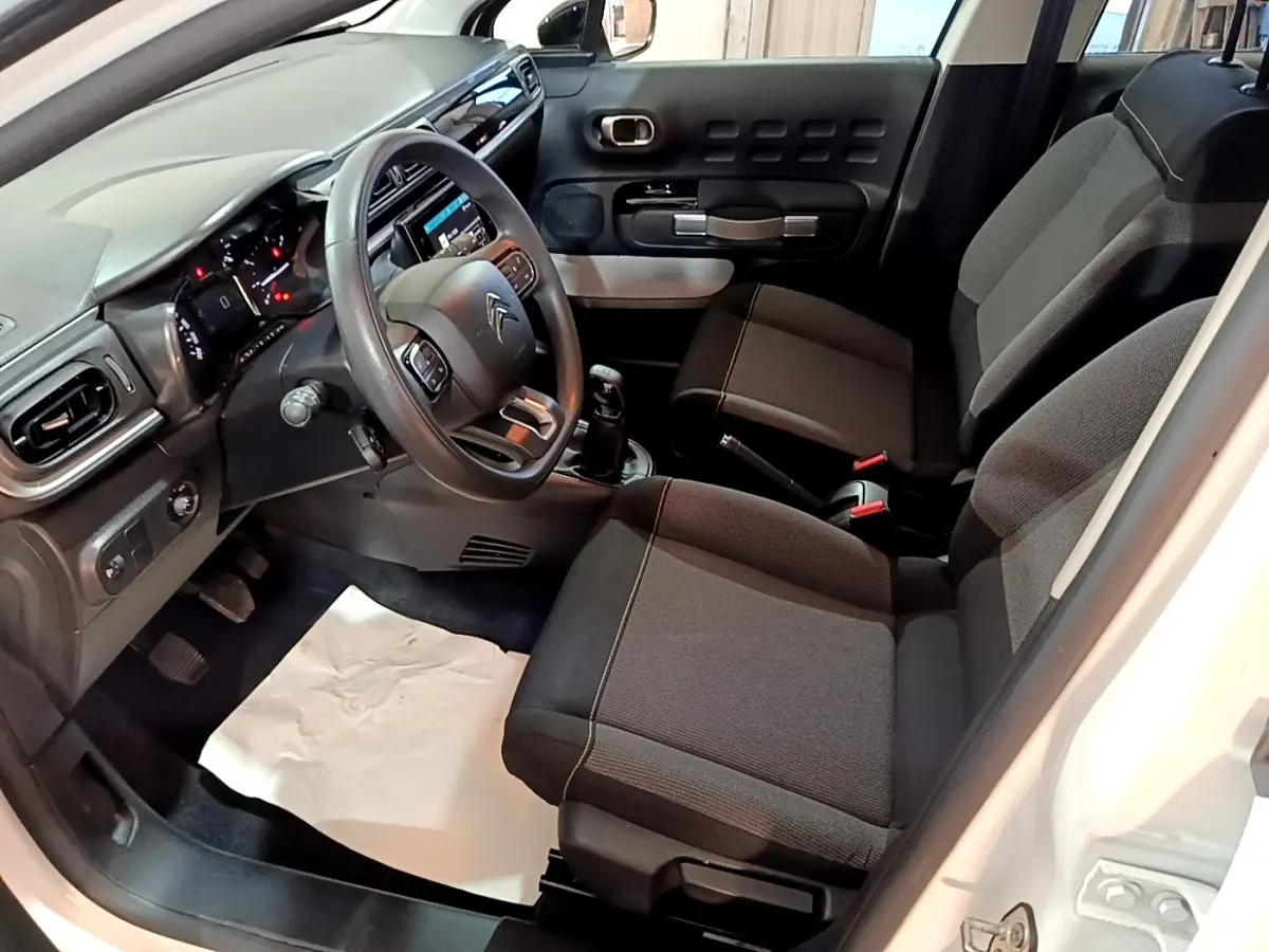 Vue intérieure côté conducteur de la Citroën C3 blanche 2020, montrant sièges tissu gris et tableau de bord moderne.