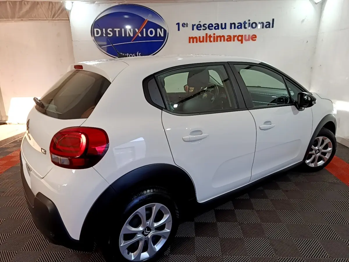 Vue 3/4 arrière droite d'une Citroën C3 blanche 2020 avec arches de roues noires et jantes alliage en showroom.