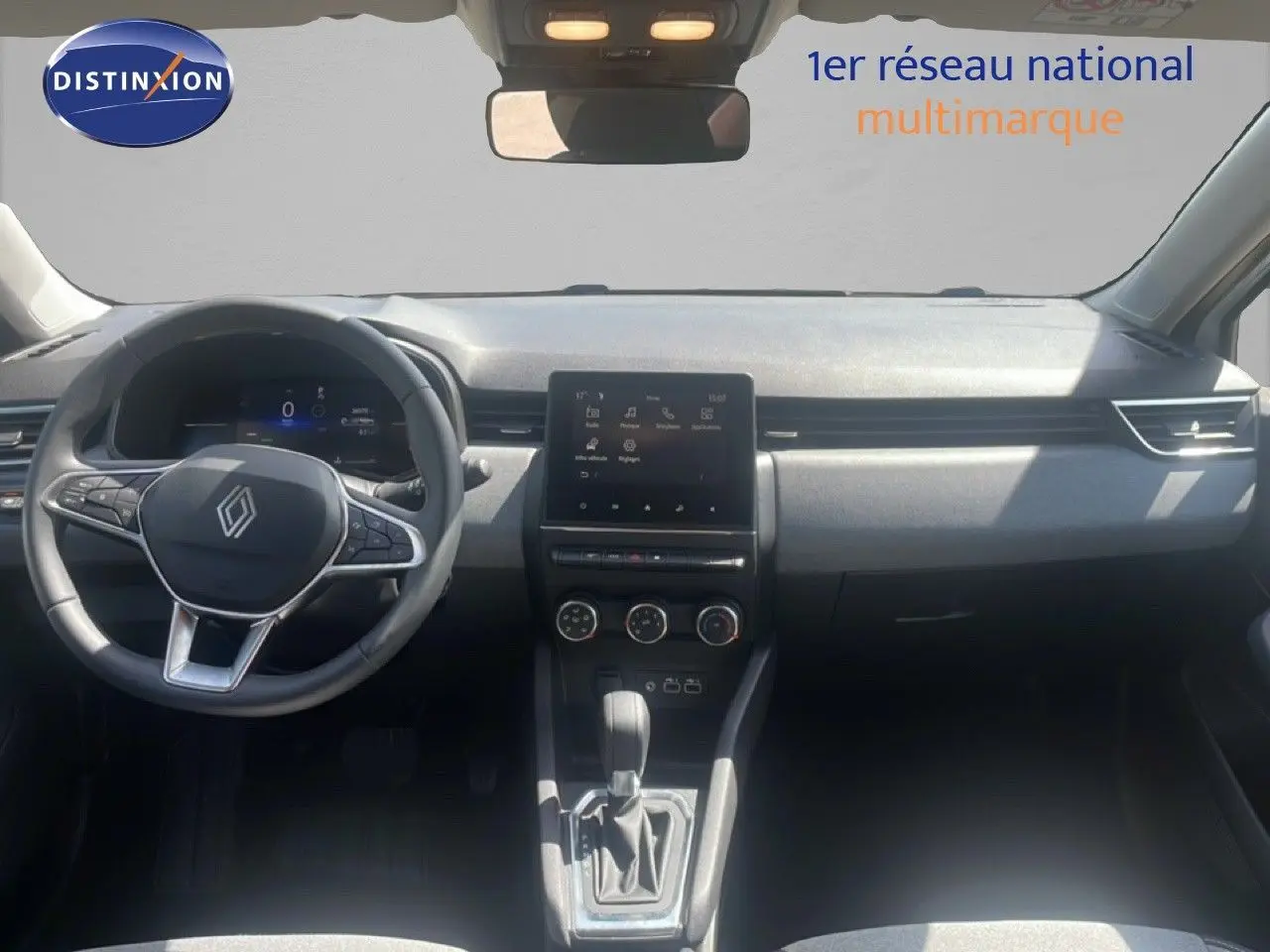 Vue intérieure avant de la Renault Clio blanche 2025, tableau de bord moderne avec écran tactile central et volant multifonction.
