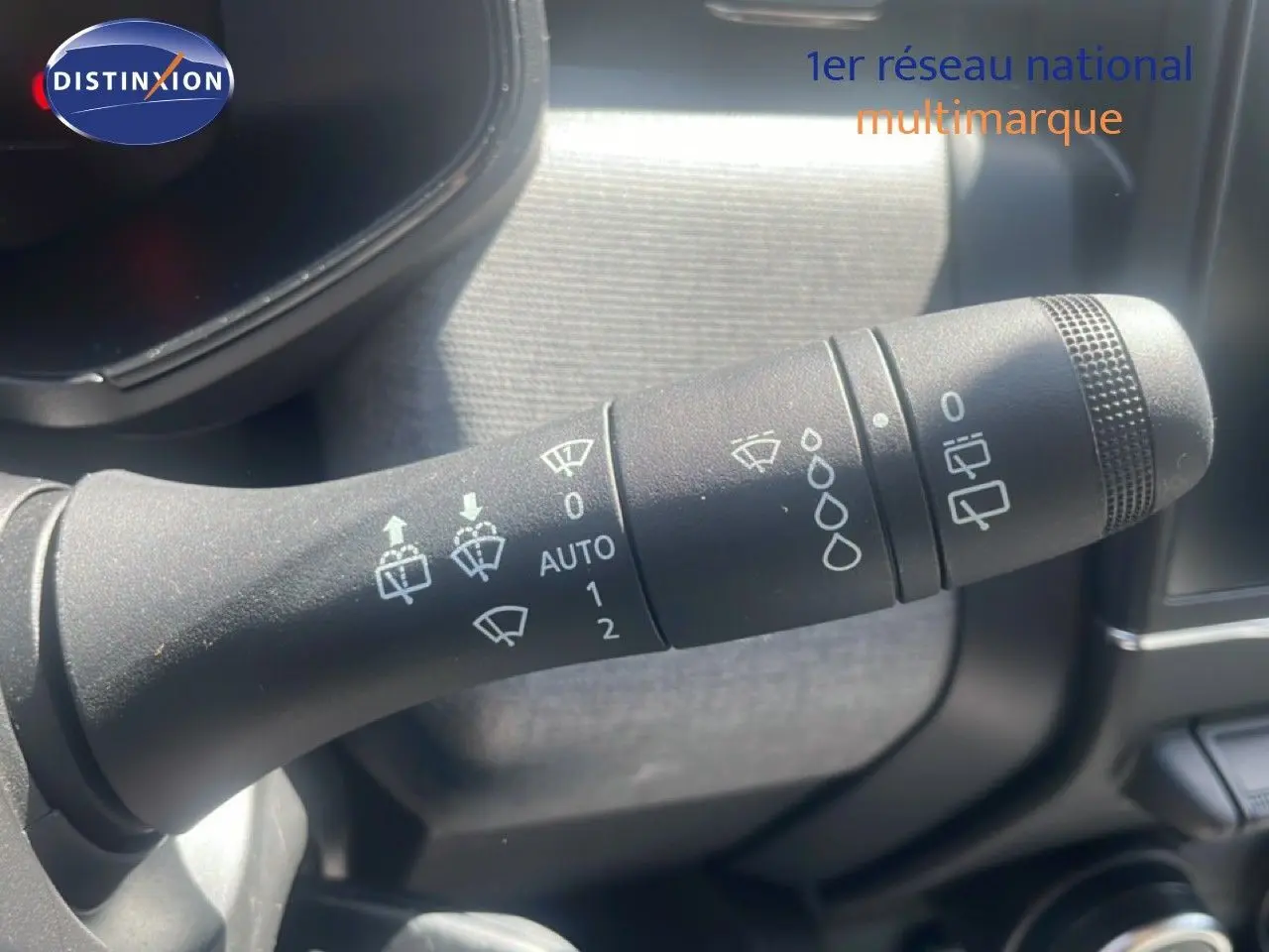 Gros plan sur la manette des essuie-glaces à l'intérieur d'une Renault Clio blanche, détails des pictogrammes visibles.