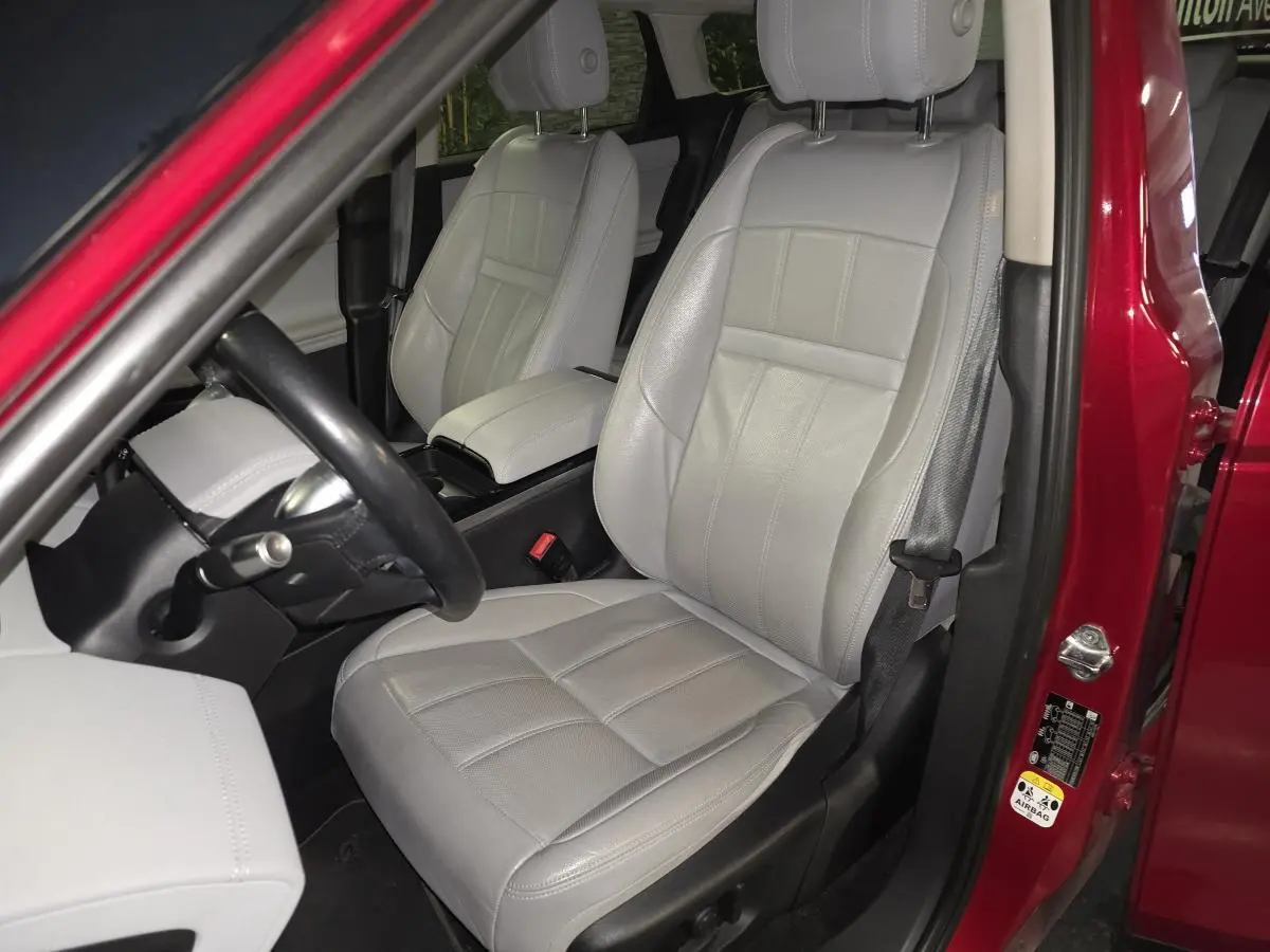 Vue intérieure côté conducteur du Range Rover Evoque rouge de 2019, avec sièges en cuir gris clair et volant noir.