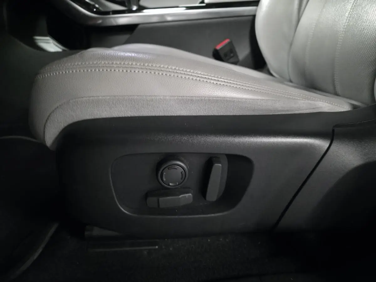 Détail du siège avant en cuir gris clair avec commandes électriques sur le côté droit du Range Rover Evoque rouge.