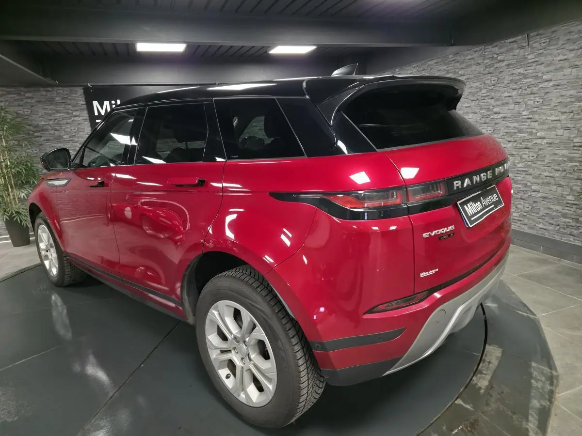 Vue 3/4 arrière droite du Range Rover Evoque rouge avec toit noir et jantes argentées en intérieur showroom.