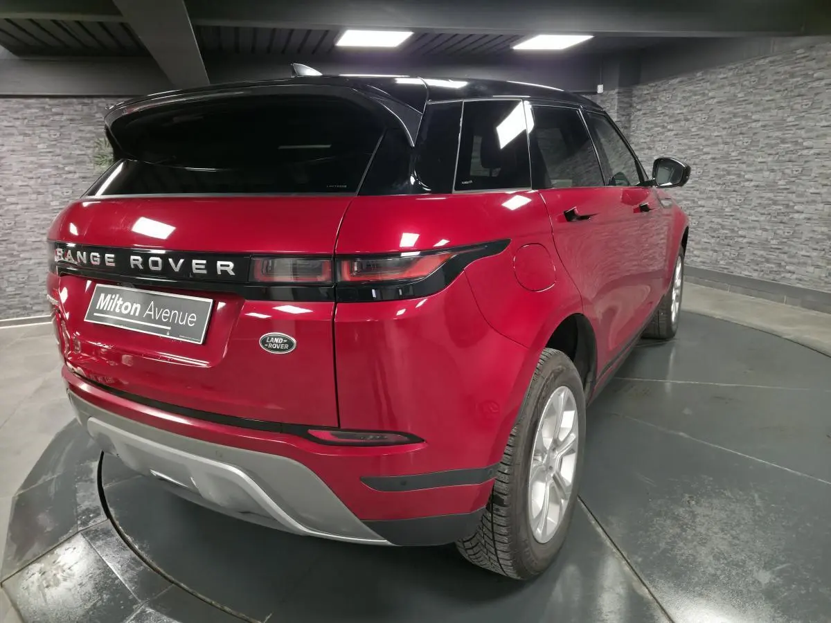Vue 3/4 arrière droite d'un Range Rover Evoque rouge avec toit noir et jantes argentées dans un showroom.