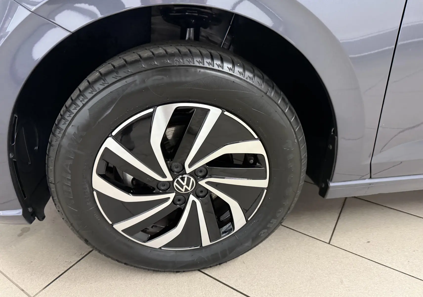 Gros plan sur la roue avant gauche avec jante alliage bicolore noire et argentée du Volkswagen Polo gris cendre.