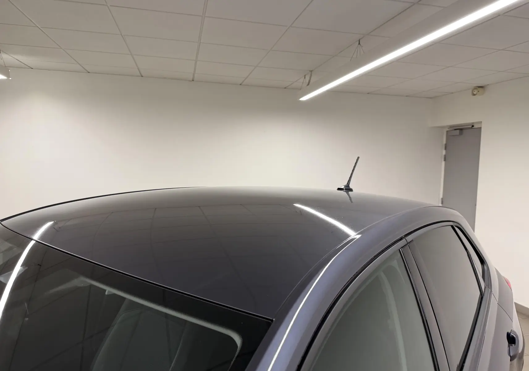 Vue rapprochée du toit gris cendre de la Volkswagen Polo 2025 avec antenne et vitres teintées dans un intérieur blanc.